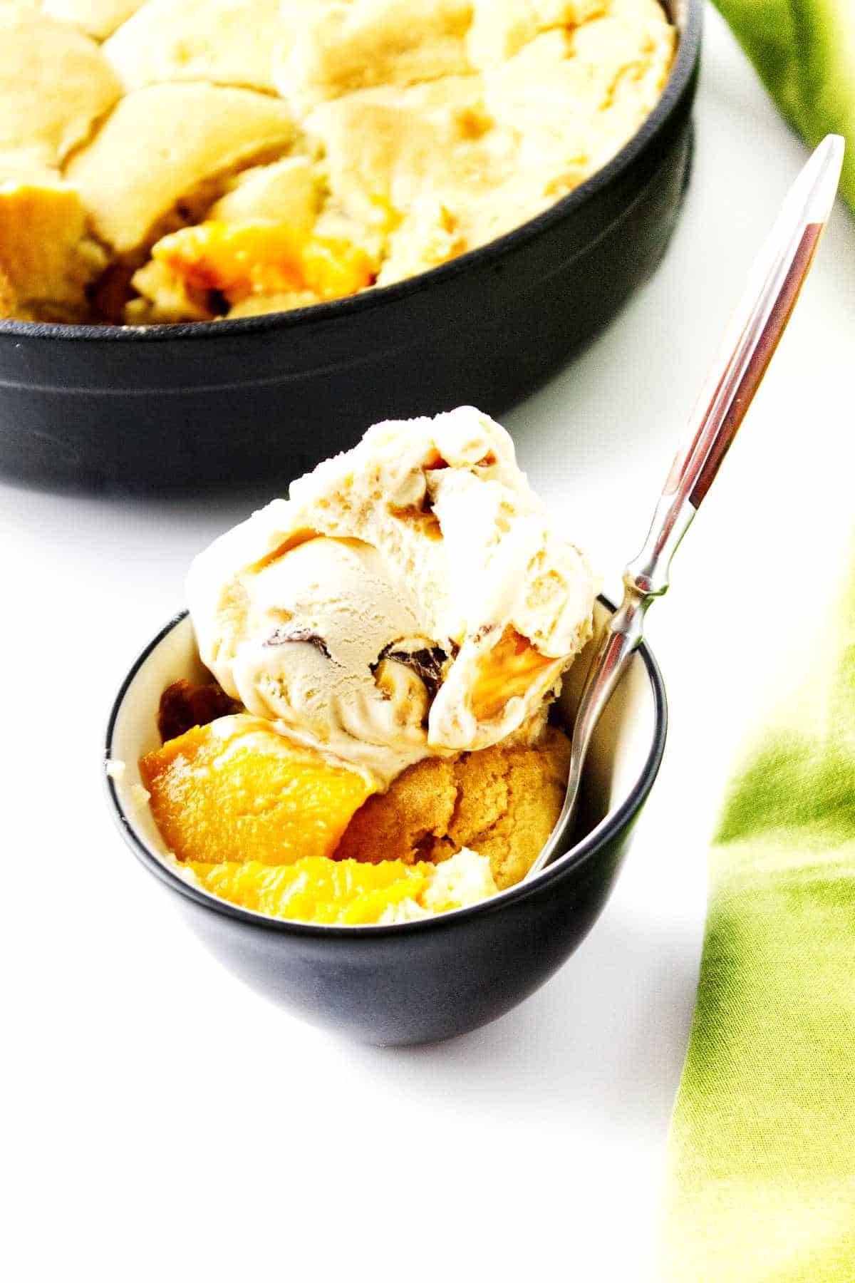 peach cobbler in a bowl with ice cream on top.