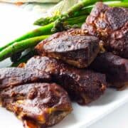 white platter of bbq boneless pork ribs with asparagus on white plate.