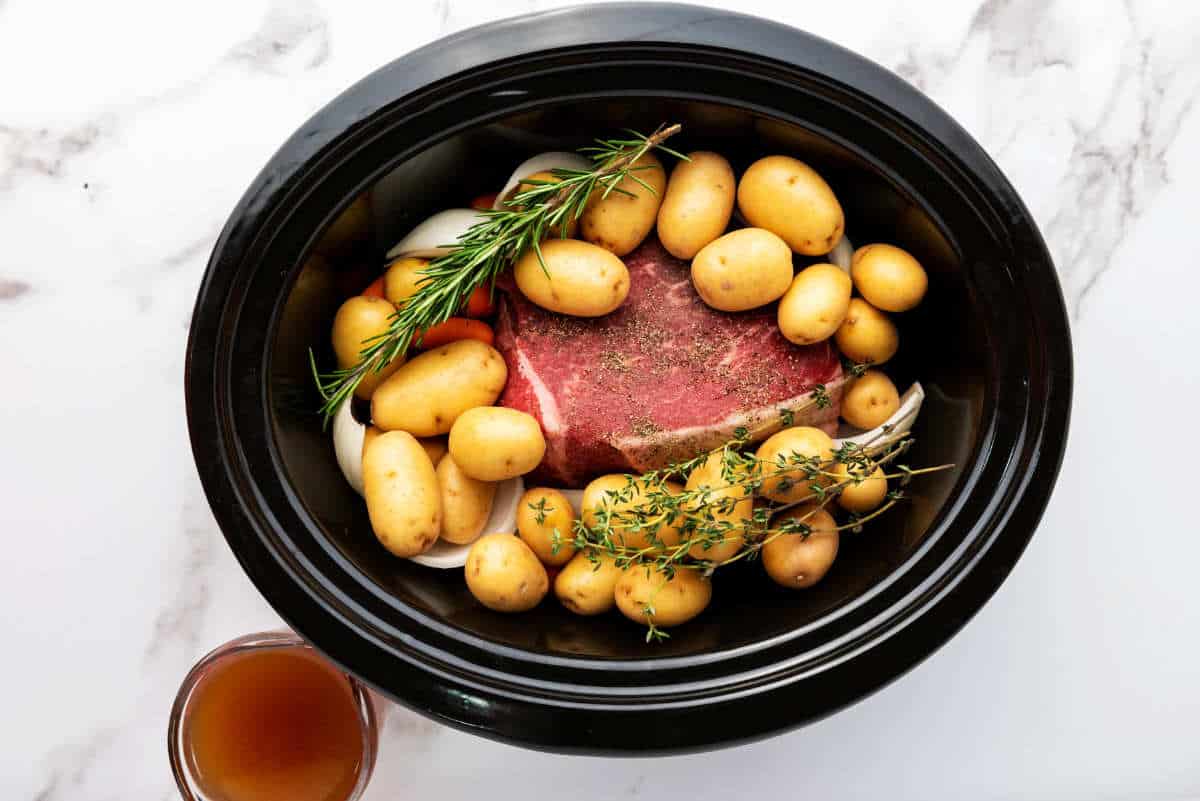 herbs, vegetables, and meat in a slow cooker.