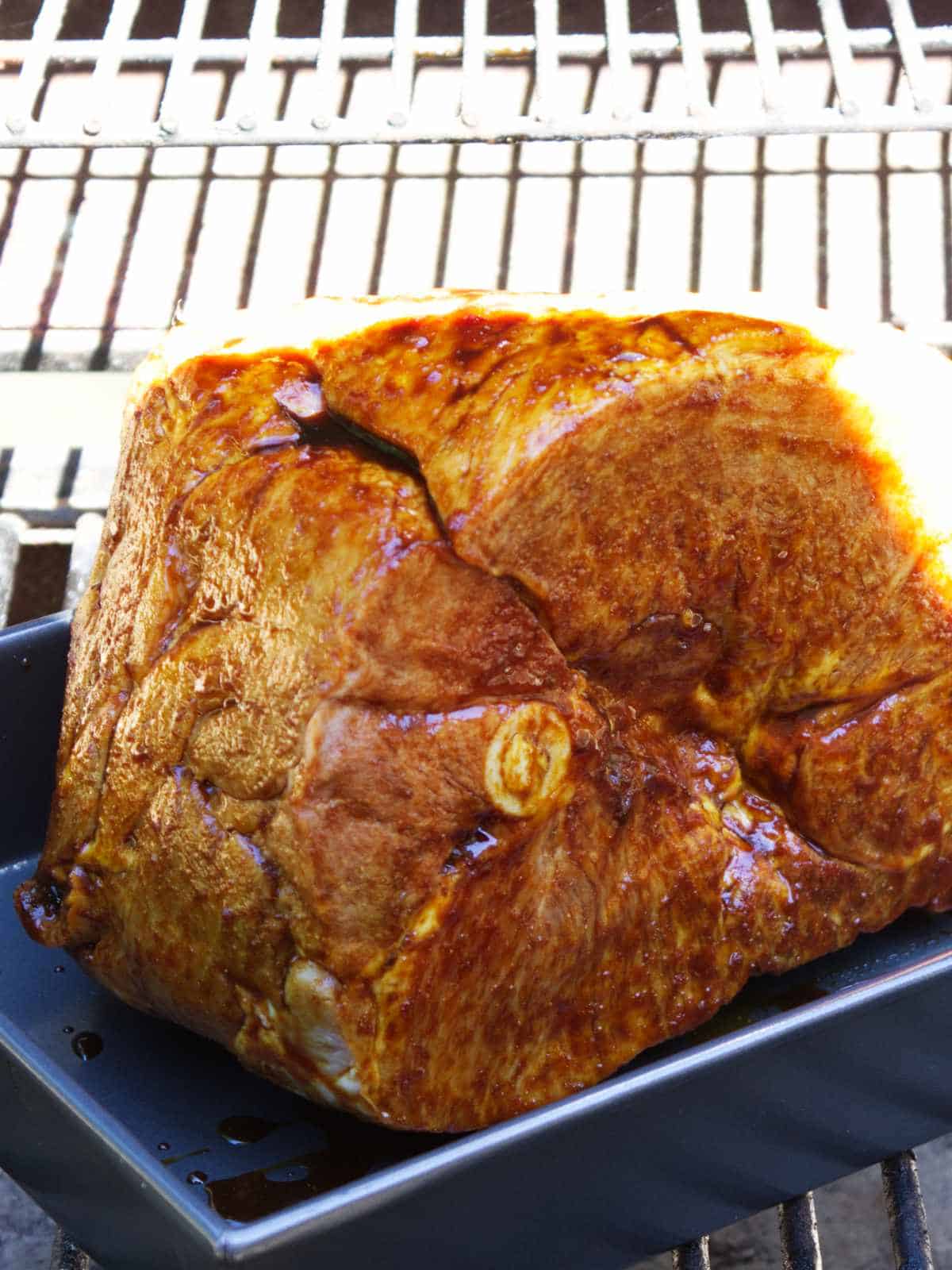 roasting pan with ham set in a grill or smoker to heat up.