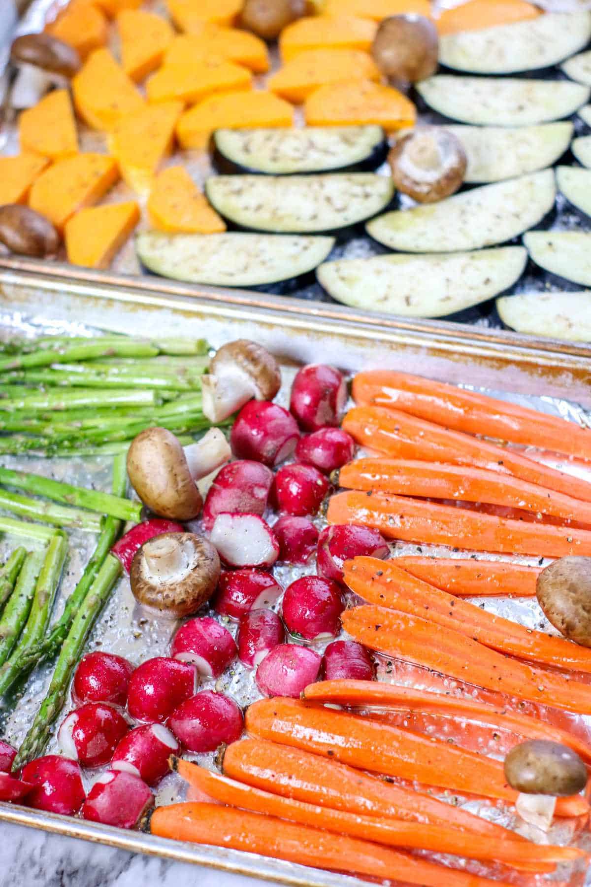 sheet pans coated with aluminum foil with seasoned raw vegetable spread out on them.