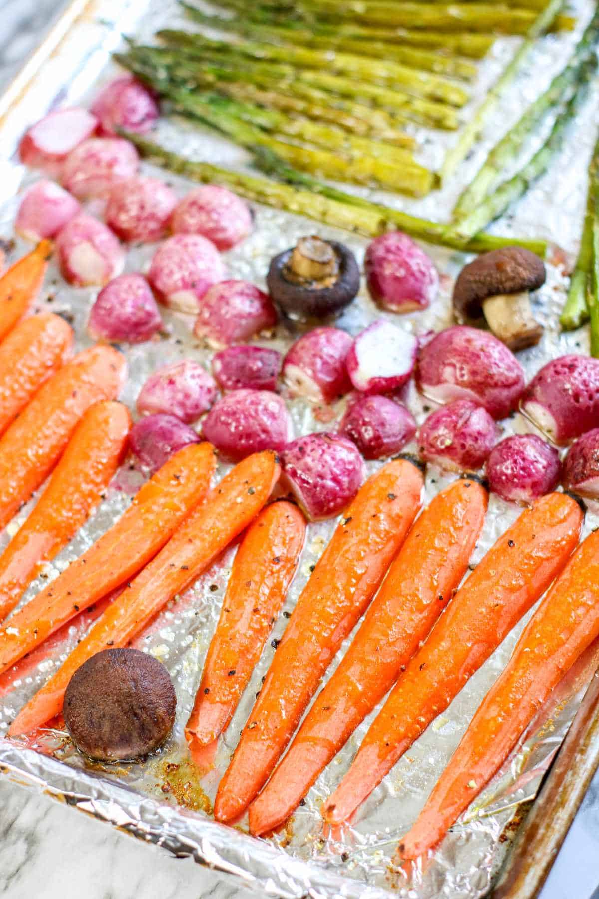 sheet pans of cooked carrots, radish, and asparagus.