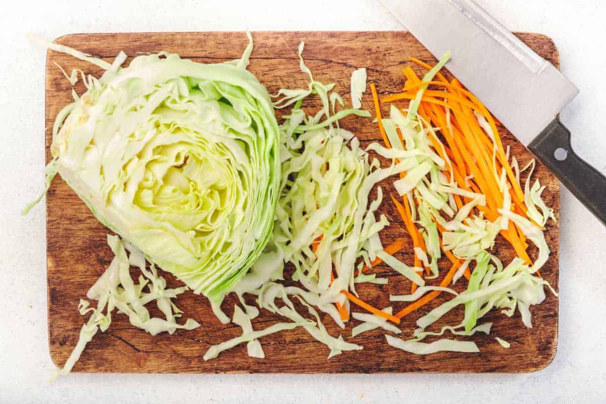 chopped cabbage and carrots on a wooden cutting board.