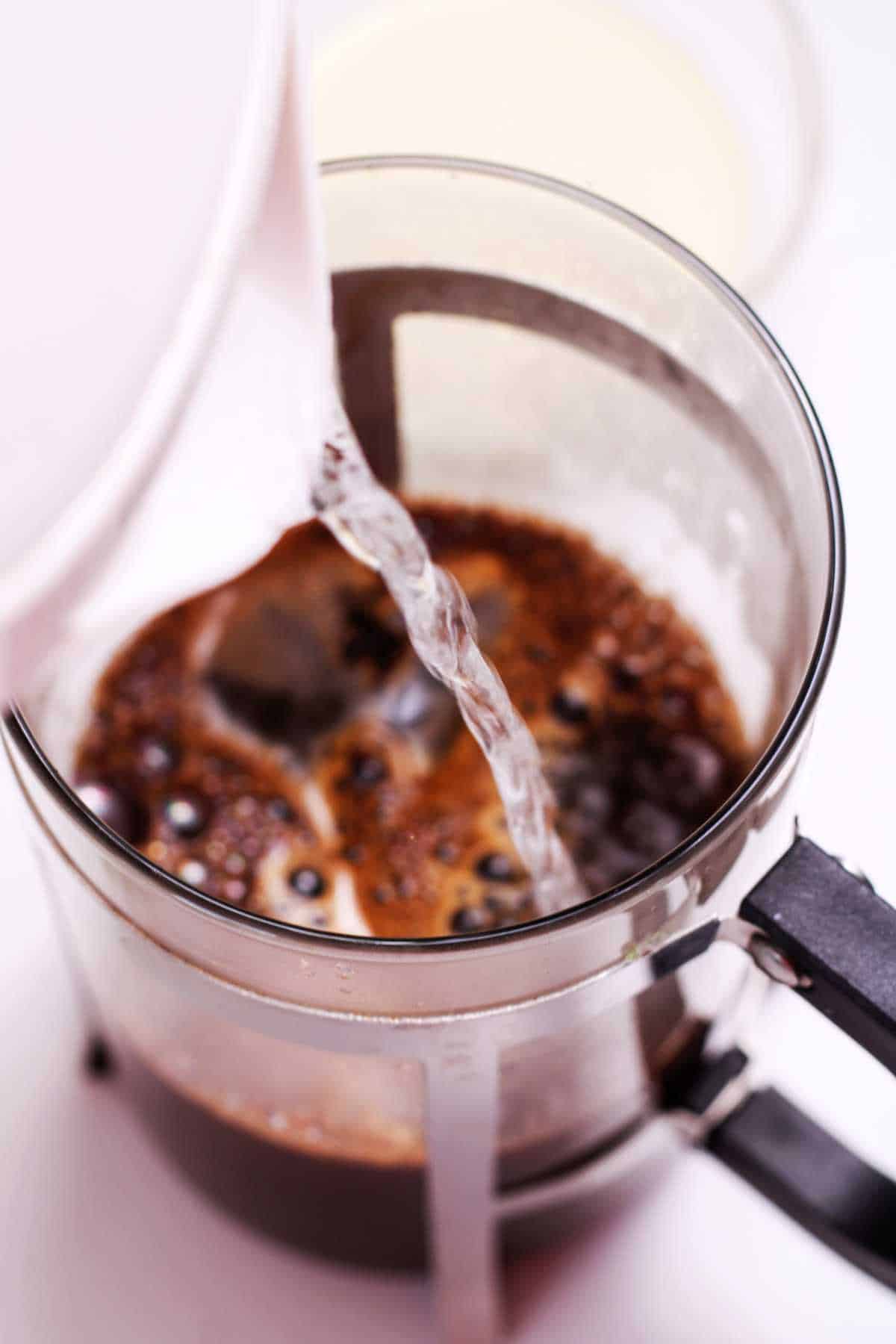 pouring hot water into a French Press with coffee grounds.