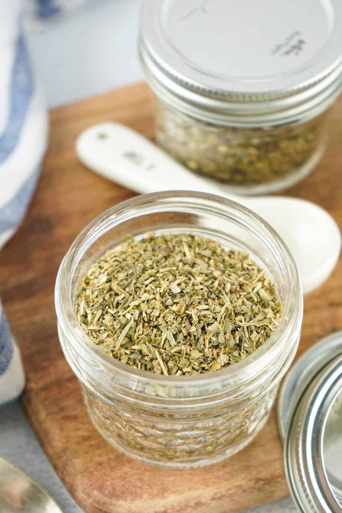 spoonful of dried herbs on a board with Italian seasoning in a small mason jar.