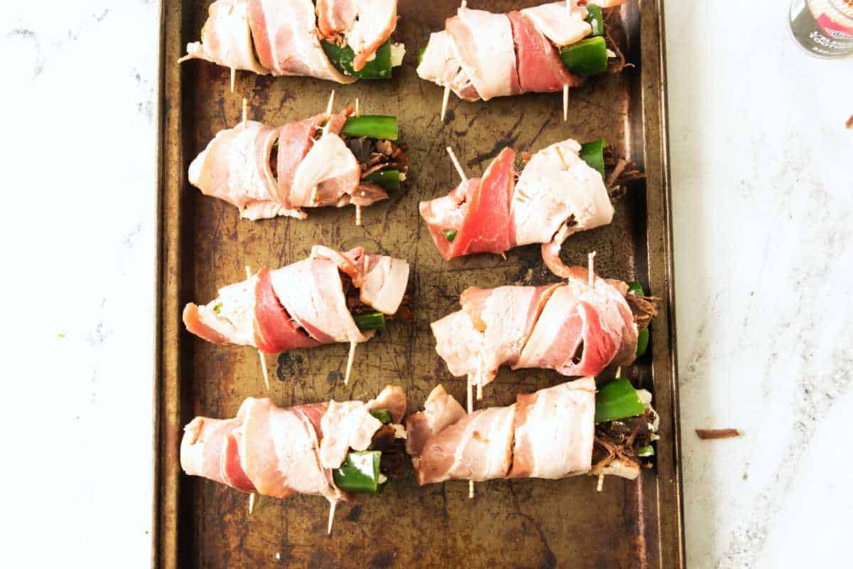 bacon wrapped, brisket filled, jalapeno poppers secured with tooth picks on a baking sheet.