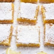 lemon bars with graham cracker crust on white parchment with powdered sugar sprinkled on them.