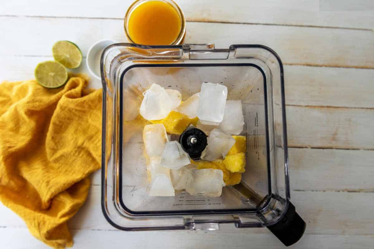ice cubes add to a blender with fruit.