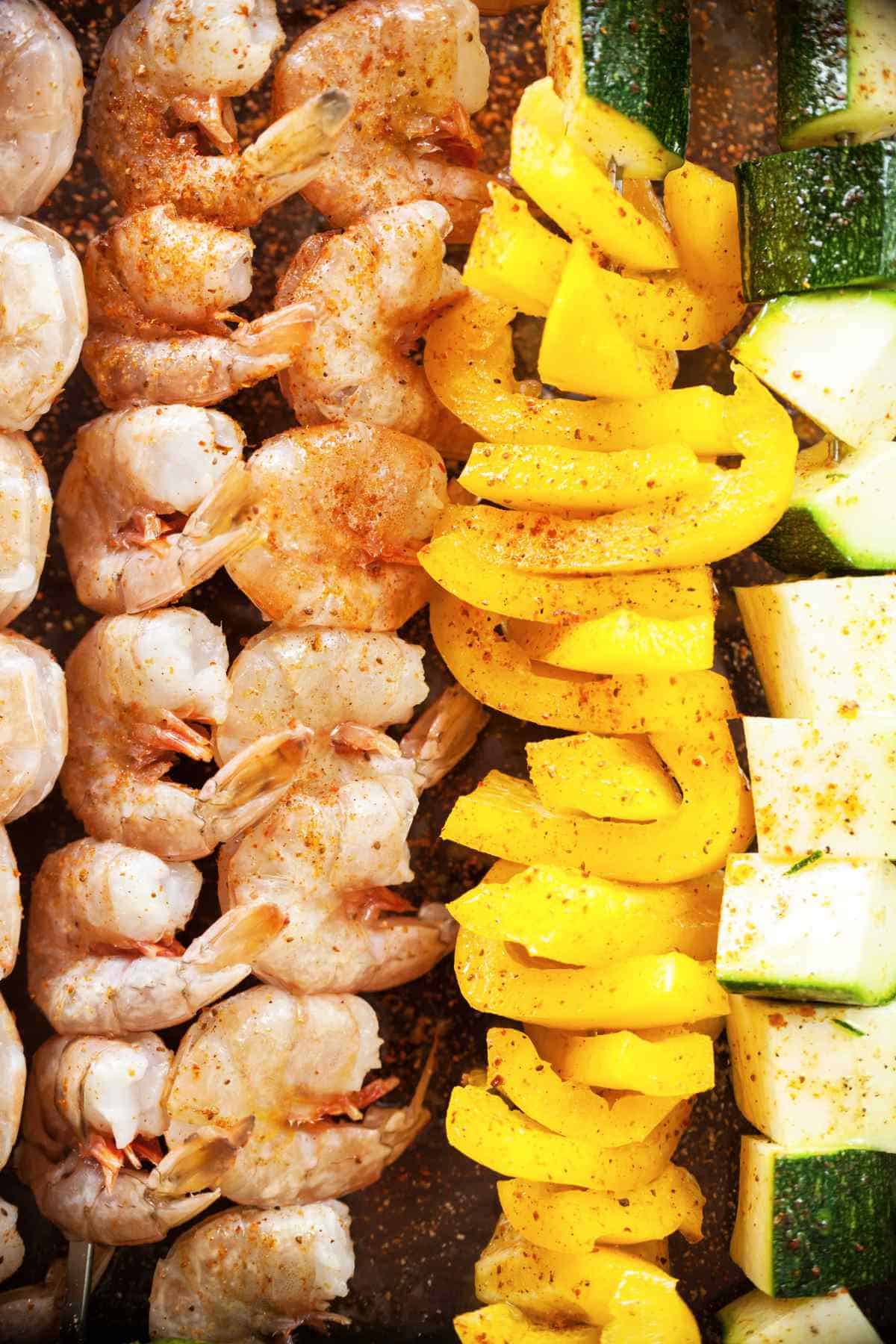 shrimp threaded on sticks next to yellow peppers and zucchini threaded on sticks.
