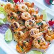 platter of oven shrimp skewers with salad, red onion slices, and lime wedges.