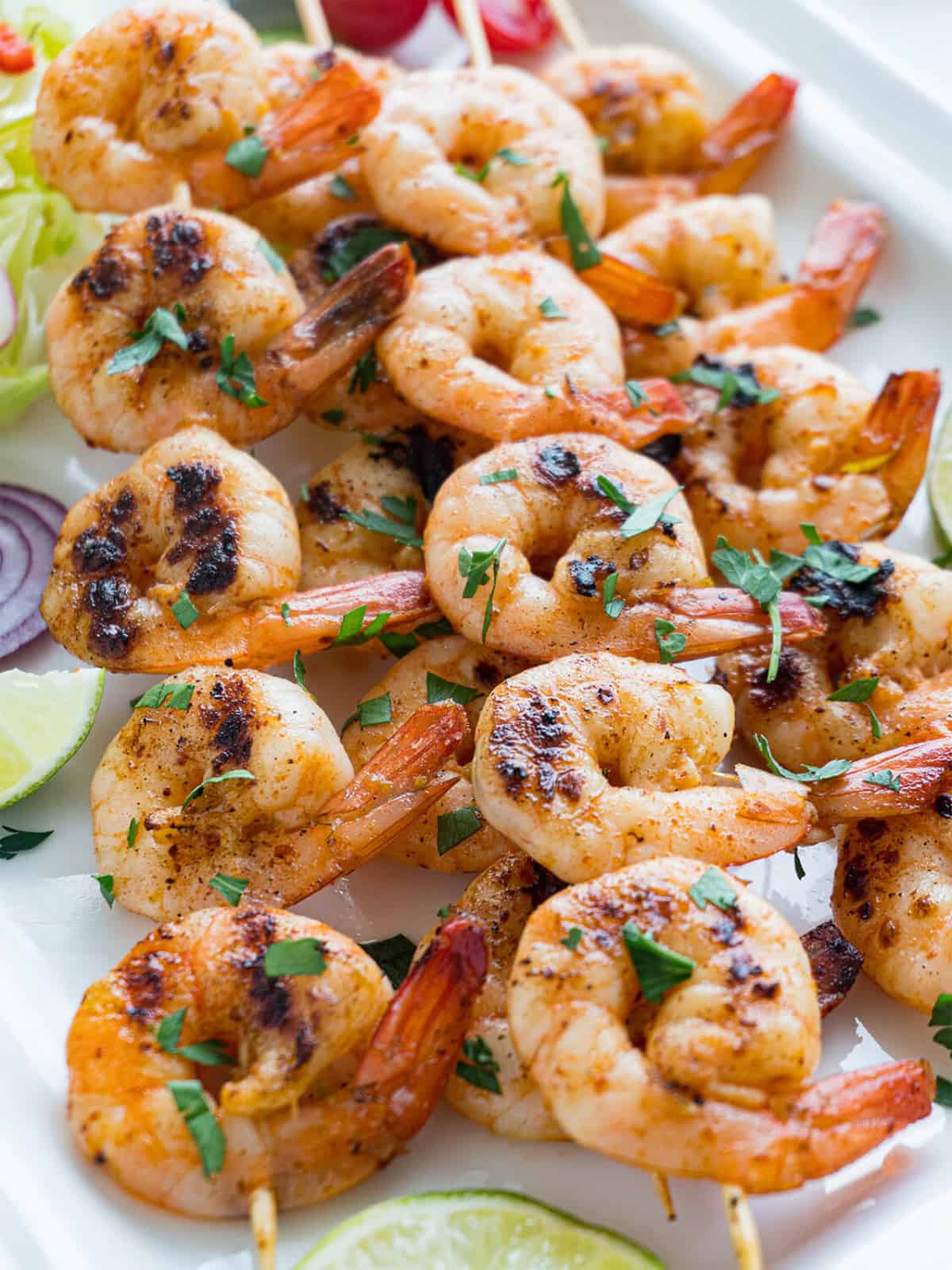 platter of oven shrimp skewers with salad, red onion slices, and lime wedges.