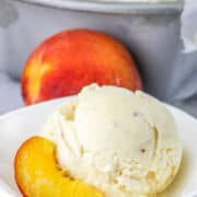 peach ice cream in a bowl with pan of frozen ice cream nearby.