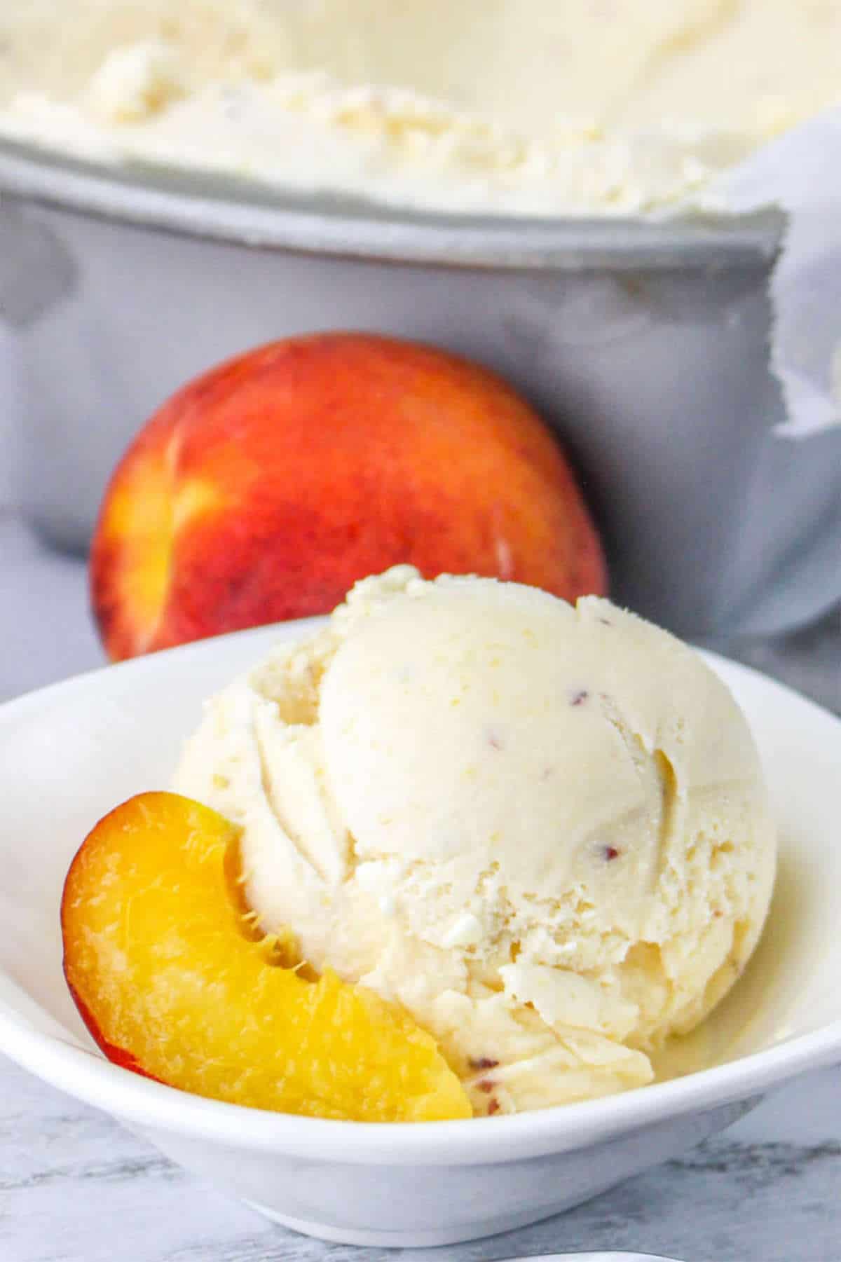 peach ice cream in a bowl with pan of frozen ice cream nearby.