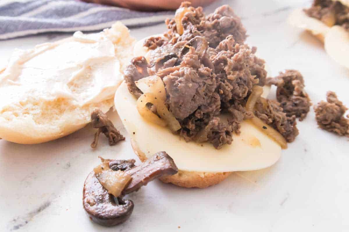 cooked shaved steak on a bun with cheese, mushrooms,a and onions.
