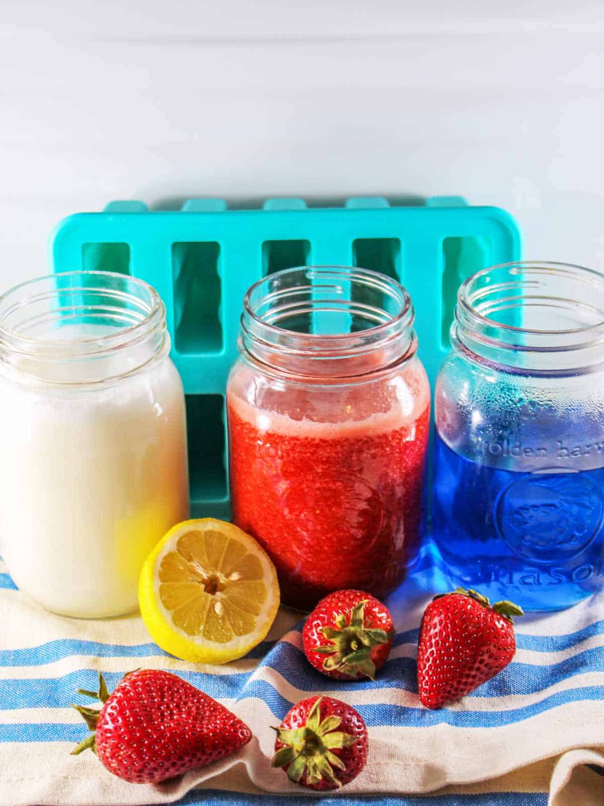 jars with coconut cream, strawberry puree, and blue raspberry jello with popsicle mold nearby.