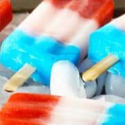 Red, white and blue popsicles with wooden sticks lay on ice, partially melting.