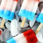 Red, white, and blue popsicles with wooden sticks are arranged on a bed of ice. The frosty popsicle red white and blue stripes highlight their frozen texture and refreshing chill.