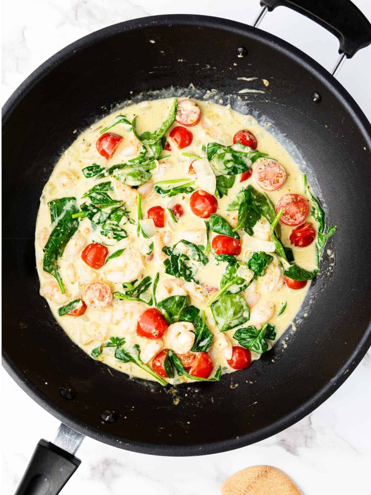 cherry tomatoes and spinach added to skillet of cream and shrimp.