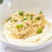 bowl of mashed potatoes with helping of chicken and gravy and garnished with parsley.