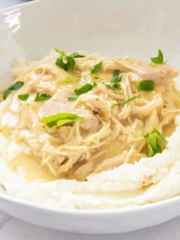 bowl of mashed potatoes with helping of chicken and gravy and garnished with parsley.
