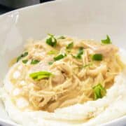 bowl of mashed potatoes with helping of chicken and gravy and garnished with parsley.