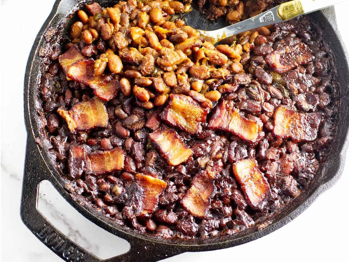cast iron skillet full of smoked baked beans with bacon on top.