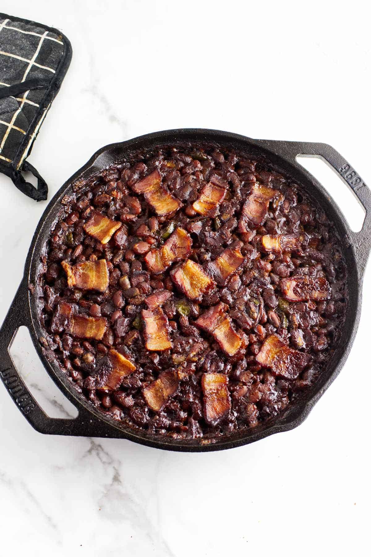 bean casserole topped with bacon in a cast iron skillet.