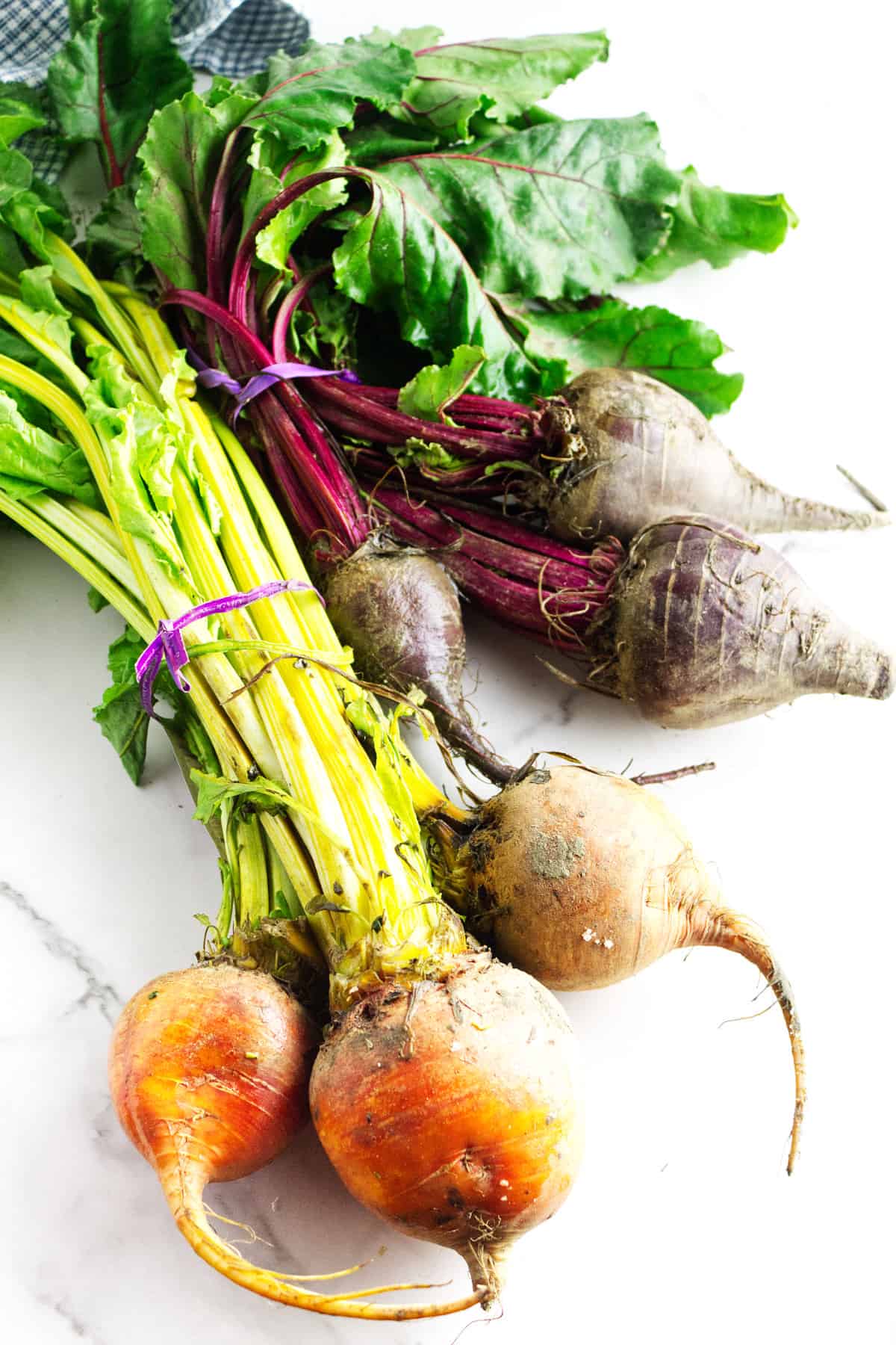 two bundles of fresh golden and red beets with stems and greens on them, on a white background.