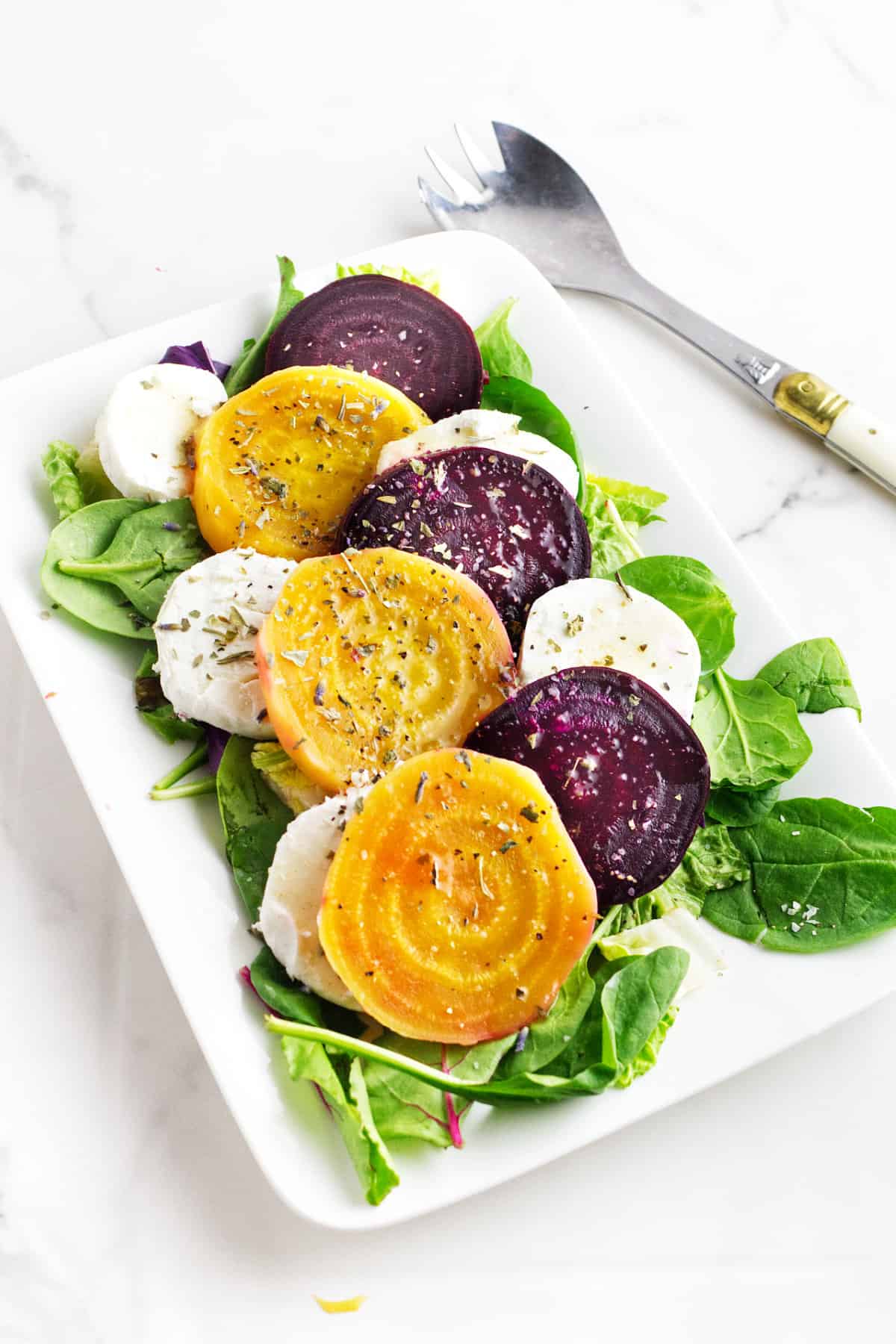 white platter with arugula and sliced beets with goat cheese.