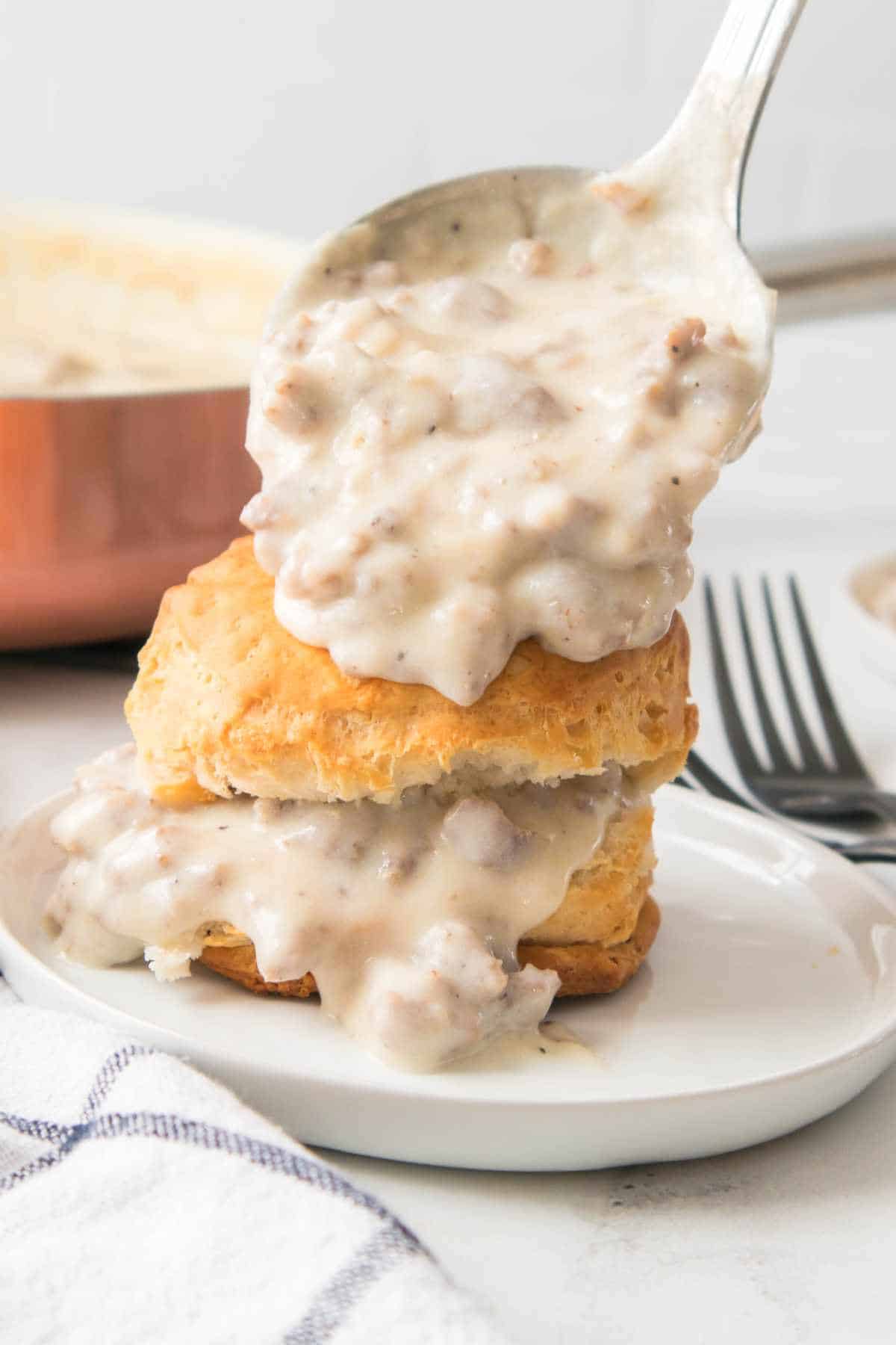 spoon ladling white pepper gravy on a biscuit.