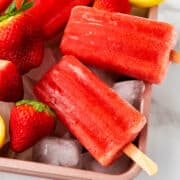 ice on a tray with strawberry popsicles on top.