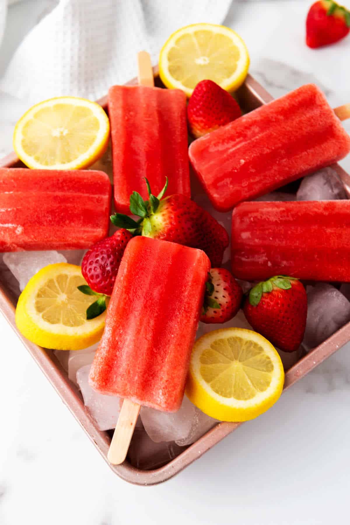 ice on a tray with strawberry popsicles on top.