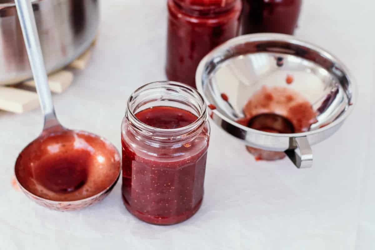 Jars of hot strawberry rhubarb jam in mason jars with ladle in canning kettle.