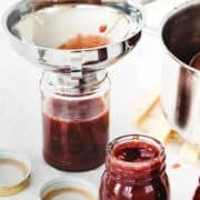 filling glass jam jars with fresh homemade strawberry rhubarb freezer jam.