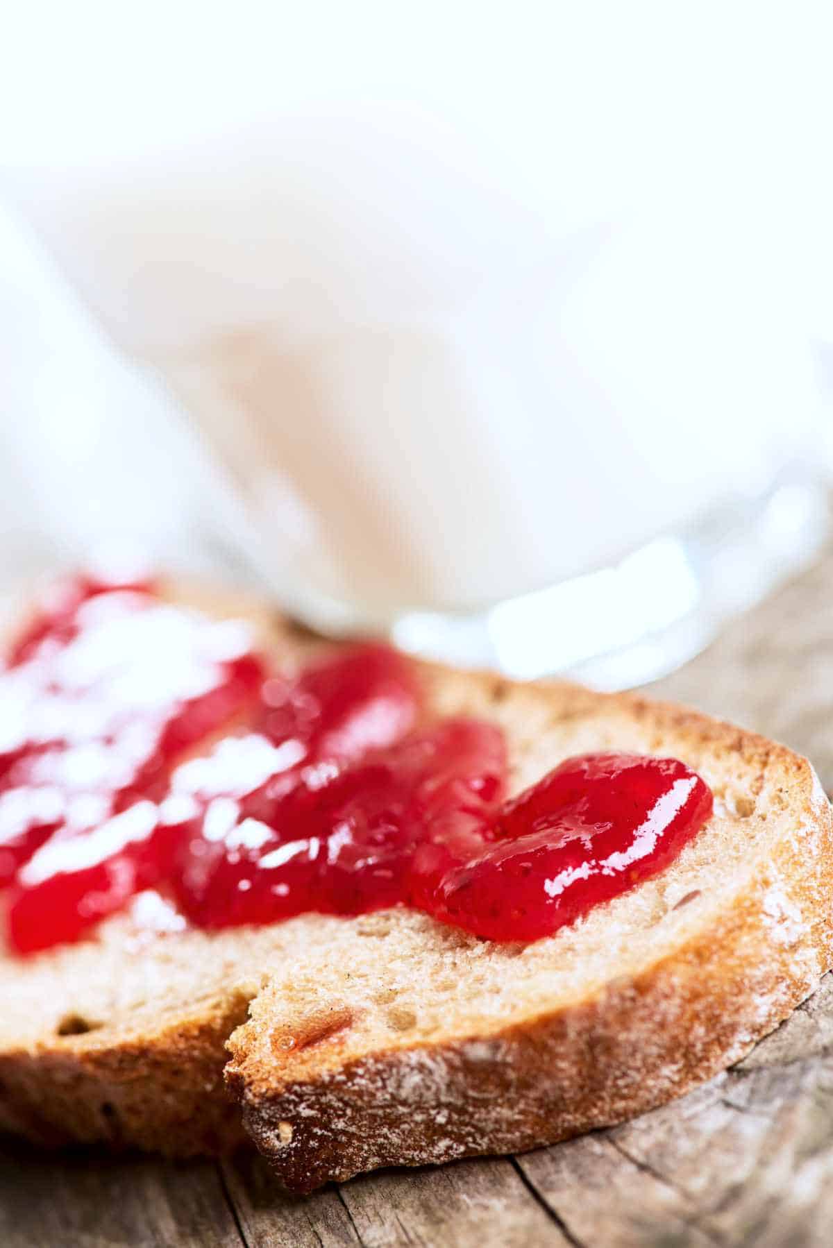 Bread with strawberry rhubarb jam and glass of milk on wooden cutting board.