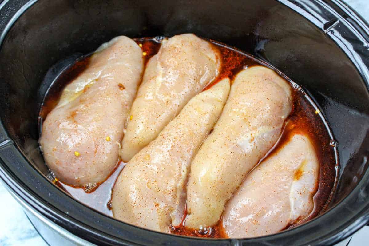 five seasoned chicken breasts in a slow cooker.