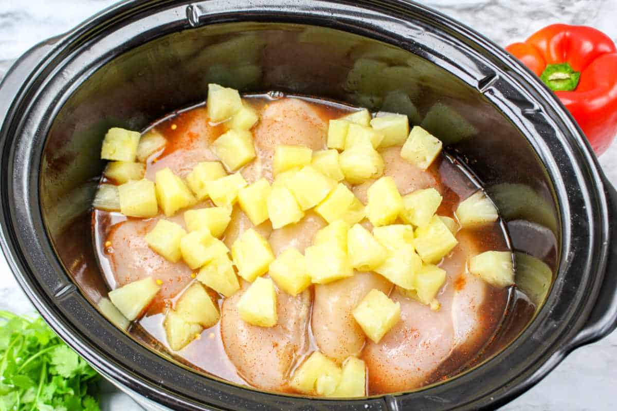 Pineapple chunks on top of chicken in a slow cooker.