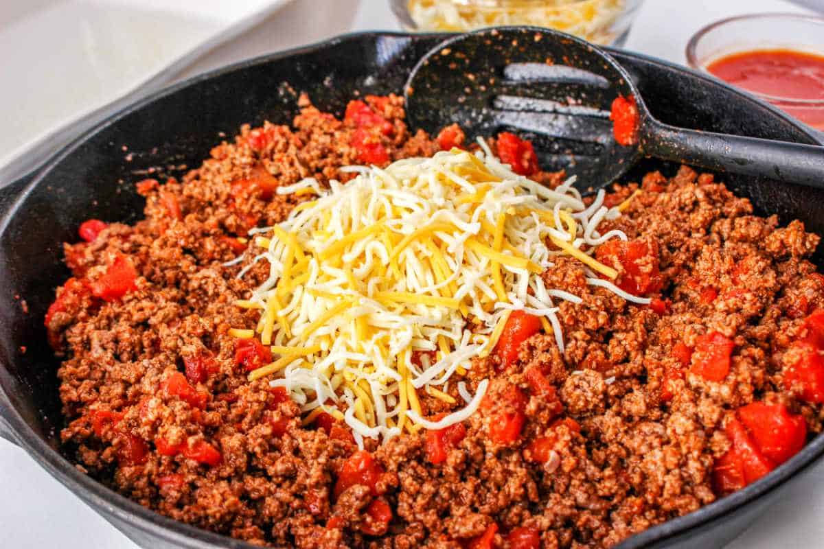 Mexican blend cheese added to ground beef mixture in a skillet.