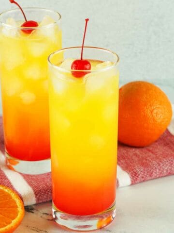 tequila sunrise on a white marble background with slices of orange nearby.