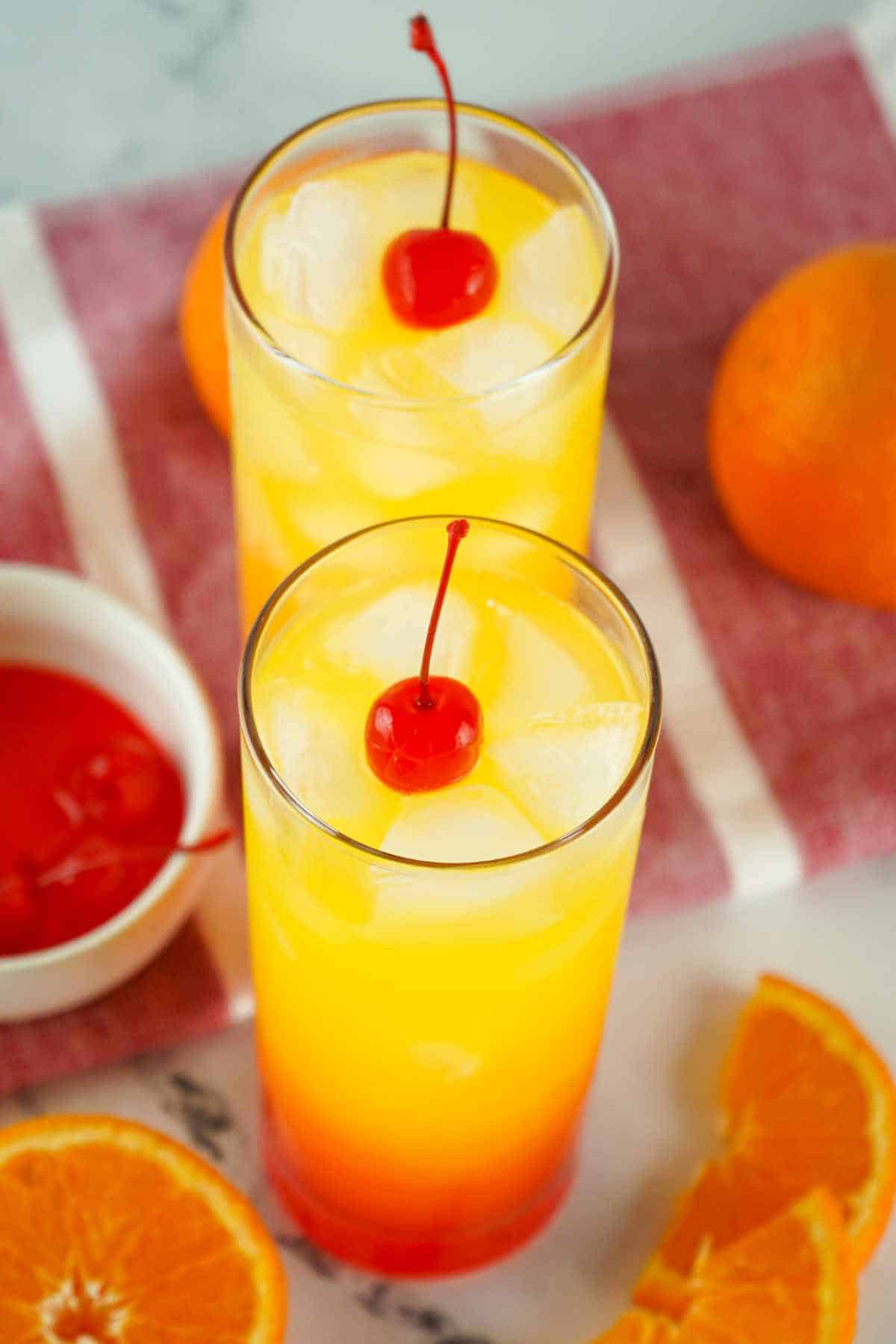 tequila sunrise on a white marble background with slices of orange nearby.