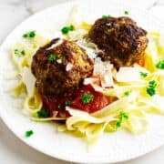 white plate with pasta and two meatballs with marinara and cheese.