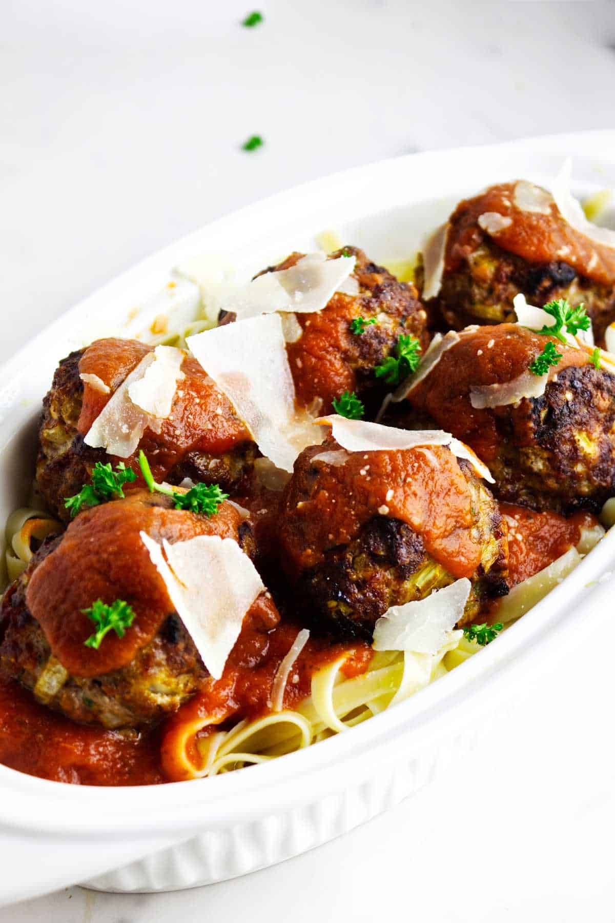 Casserole of meat balls on pasta and covered with spaghetti sauce and cheese shavings.