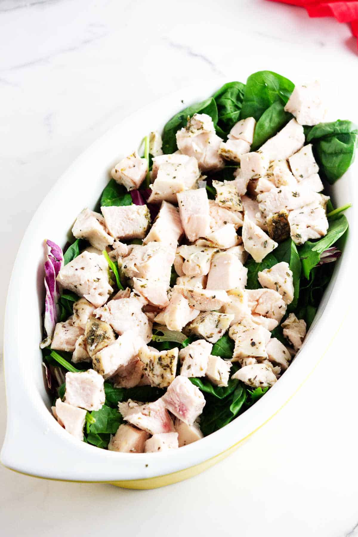 large oval platter filled with salad greens and topped with cooked, cubed chicken breast.