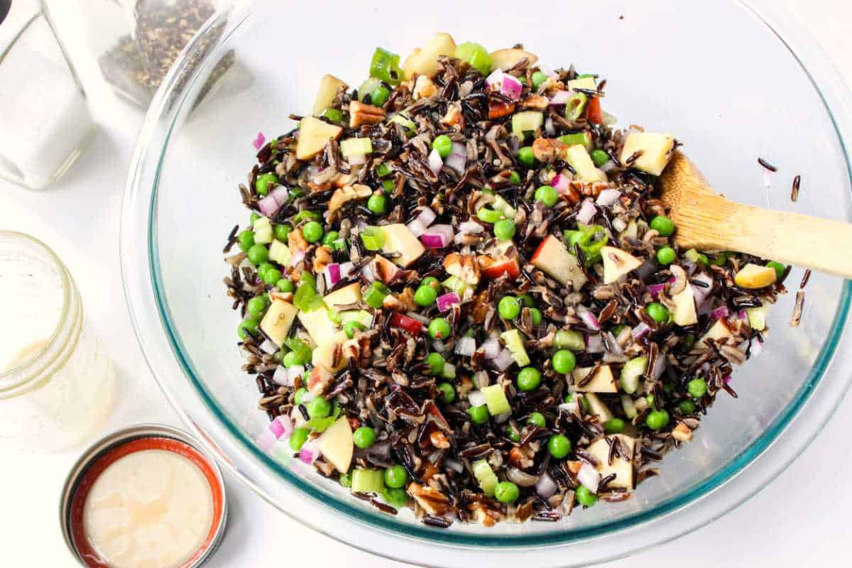 large glass bowl with salad dressing tossed with wild rice salad ingredients.