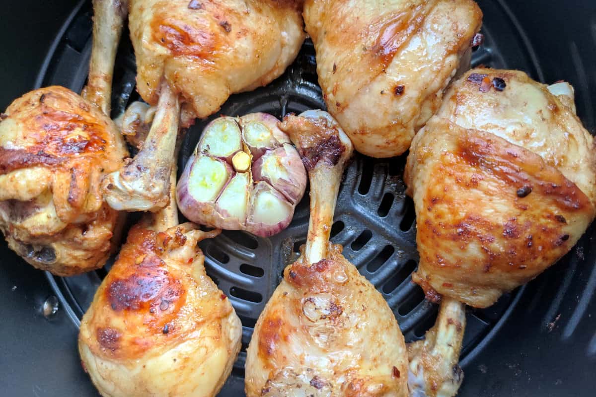 barbecued drumsticks in an air fryer with a head of garlic.