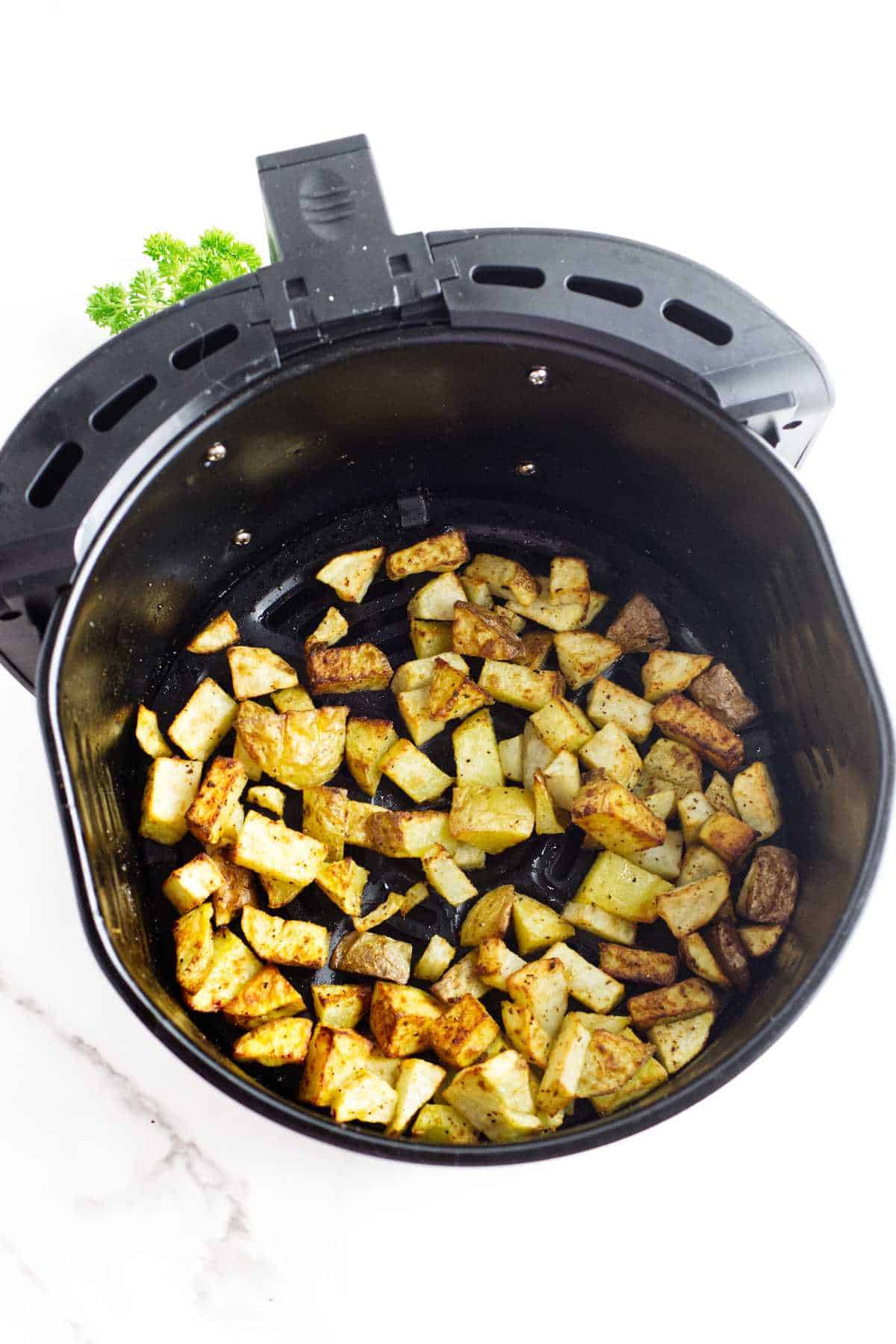 cubes of cooked potato in the basket of an air fryer.