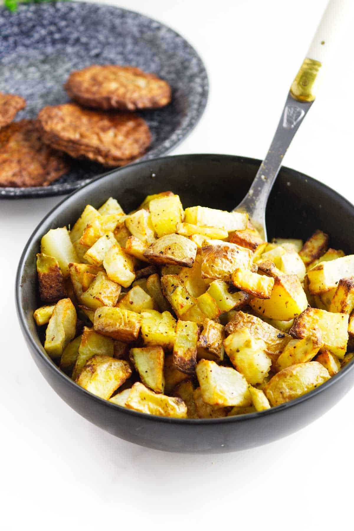 bowl of air fried diced potatoes with sausage in the background.