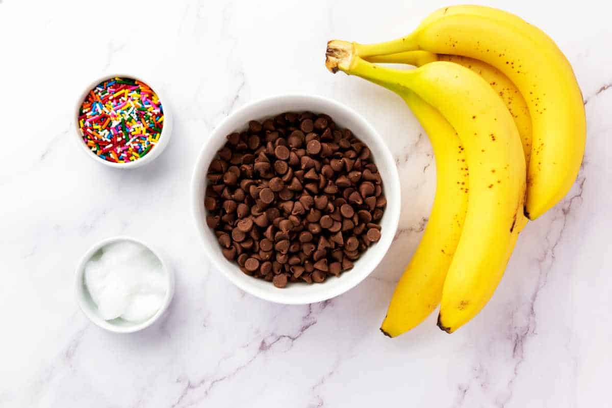 bananas, bowl of chocolate chips, small bowl of coconut oil, and a tiny bowl of colorful sprinkles.
