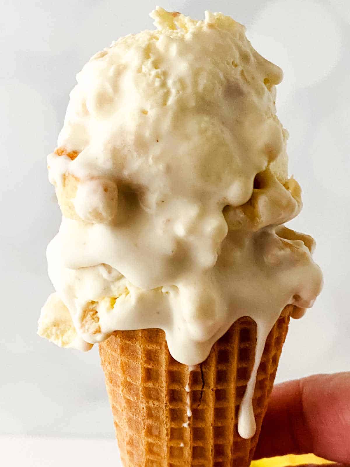 Ice cream cone with scoops of banana ice cream with some drips down the cone.