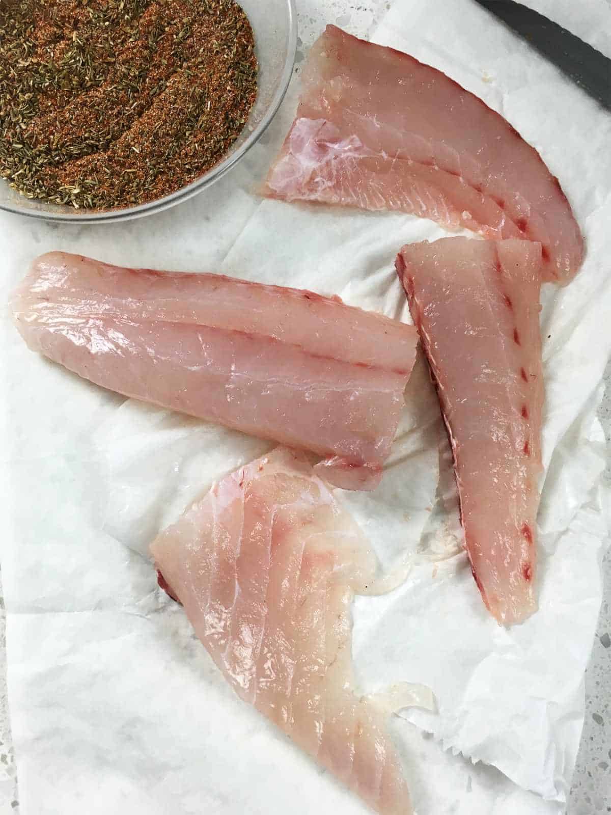 fresh grouper or snapper filets on white butcher paper with bowl of blackening seasoning nearby.